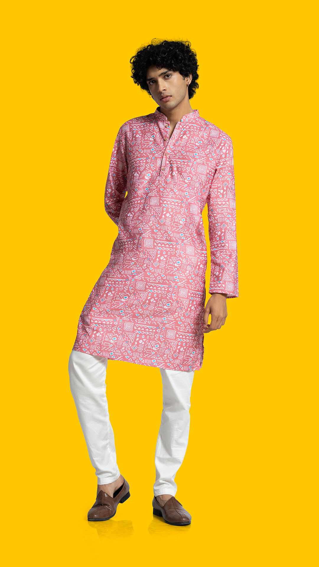 Man wearing a pink printed kurta with white churidar and loafers, showcasing elegant festive style with a modern ethnic appeal.